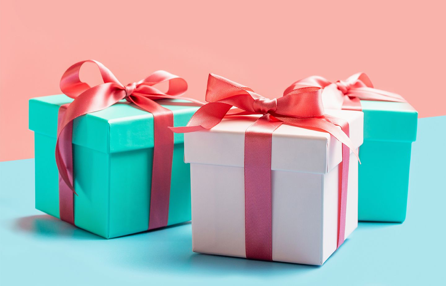 3 gift boxes tied with ribbons against peach and green background.