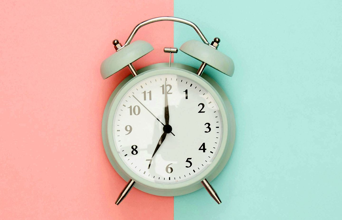 Plale green alarm clock against peach and green background.